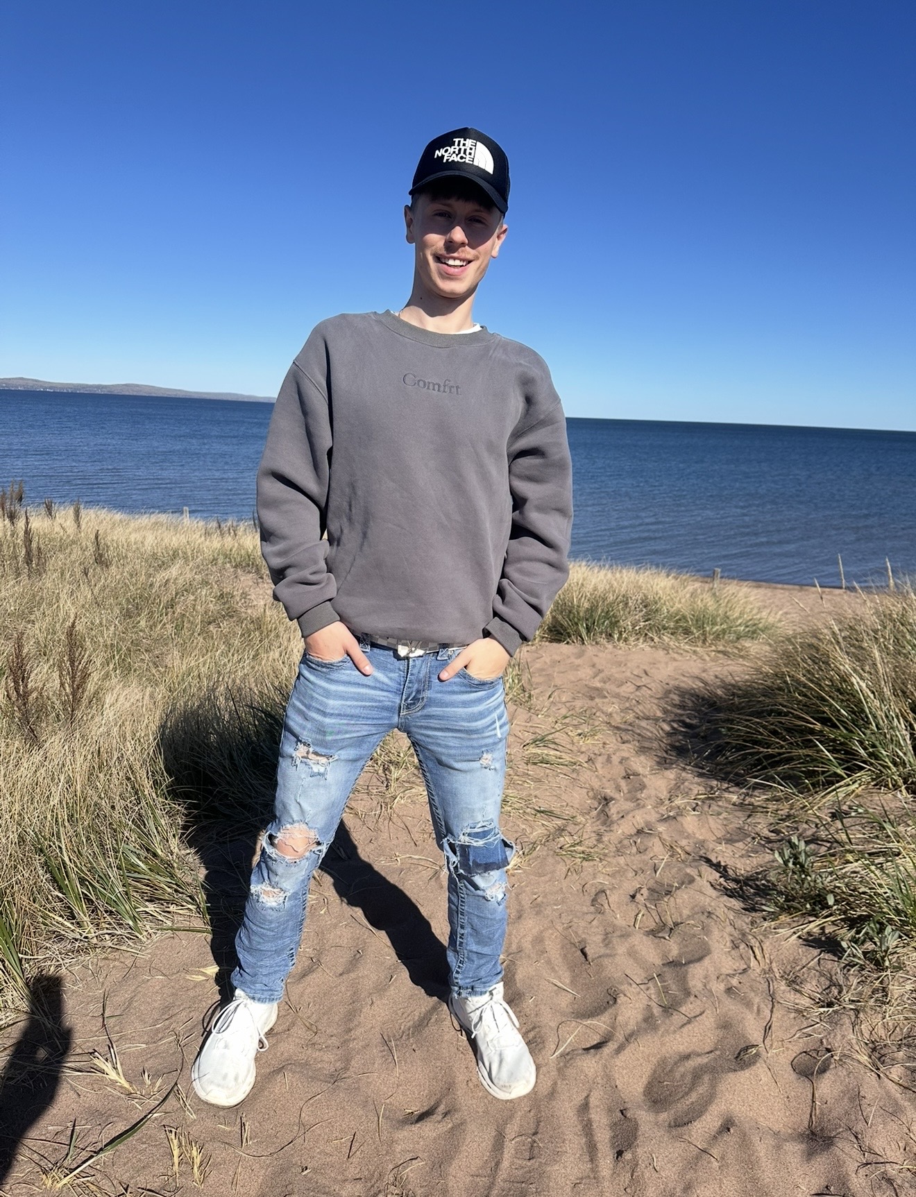 Logen standing on a sandy dune above a wide blue lake
